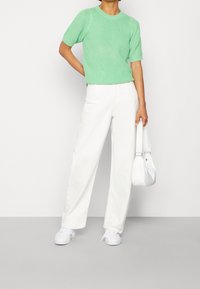 Miętowo-zielony sweter z krótkim rękawem, zestawiony z białymi spodniami z szerokimi nogawkami i białymi trampkami. Modelka trzyma małą białą torebkę.