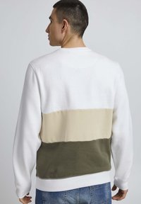 Sudadera de algodón con un diseño a bloques de color que incluye secciones en blanco, beige y verde oliva. Puños y dobladillo acanalados con detalle de costura.