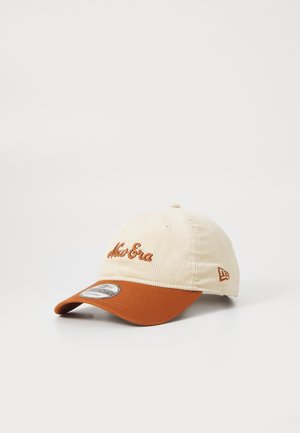 Beżowa czapka sztruksowa z brązowym daszkiem, z haftowanym napisem "New Era" na przodzie oraz logo po boku, prezentowana na białym tle.