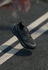 Black athletic shoe with a textured upper, featuring three stripes on the side, a rounded toe, and a cushioned sole. Light Boost technology.