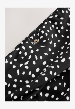 Zwarte stof met een wit gestippeld patroon en een klein, goudkleurig embleem. De textuur lijkt glad en licht reflecterend.