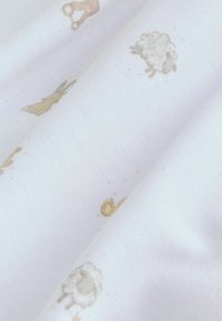 Tissu en coton blanc avec des motifs subtils d'animaux beige, incluant un lapin et un mouton, présentant une surface douce et texturée.