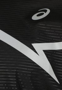 Svart atletisk tyg med horisontella och vertikala texturerade mönster. En stor vit logotyp i form av en blixtdesign är tydligt synlig.