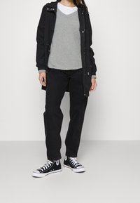 Parka noir sur un pull texturé gris clair, associé à un pantalon noir et des baskets Converse noires. Tenue simple et décontractée.