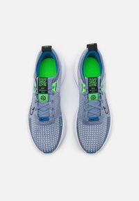 Zapatillas deportivas grises con parte superior de malla texturizada, acentos en turquesa y una etiqueta de código QR verde. La suela es blanca y tiene un diseño ligero.
