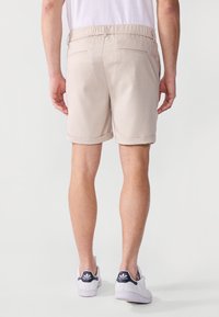Shorts beige avec une taille élastique, des ourlets roulés et deux poches arrière. Portés avec des baskets blanches ayant un accent marine.
