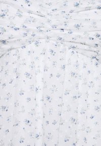 Robe fleurie avec un fond blanc, présentant des fleurs bleues et des feuilles vertes. Le tissu semble transparent avec une texture subtile et des détails froncés.