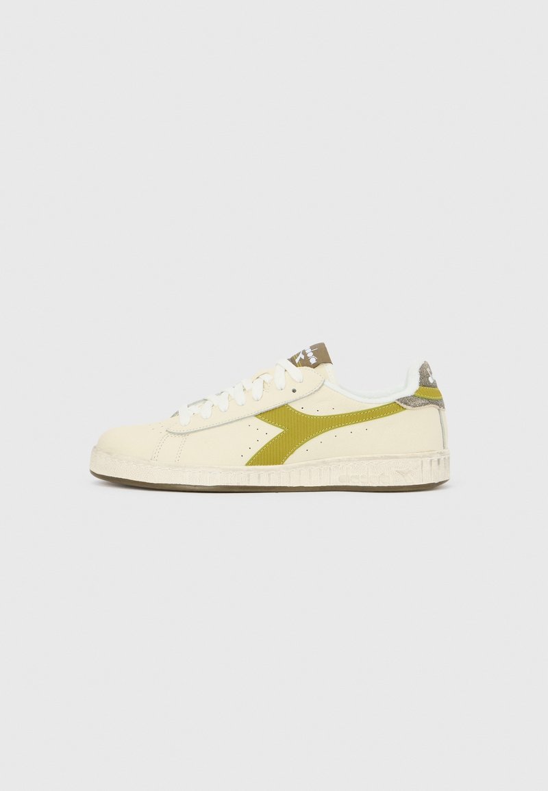 Sneaker basse crème avec lacets blancs, bande latérale vert olive, semelle blanche texturée et détail marron sur la languette et la languette arrière.