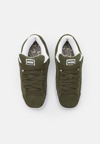 Grønn semsket sneakers med teksturerte lisser, hvit innside og mønstret såle. Inkluderer en svart logo på tungen.