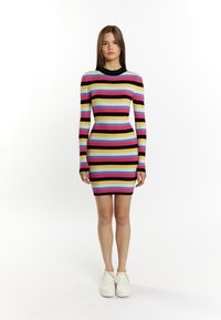 Rippstrickkleid mit horizontalen Streifen in Pink, Schwarz, Gelb und Blau. Lange Ärmel und eine figurbetonte Silhouette. Weiße Sneakers.