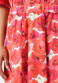 Blumenkleid mit weißem Hintergrund, das große, lebendige rote Mohnblumen und grüne Stiele zeigt. Der Stoff hat eine weiche, glatte Textur.