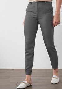 Hallused hallid püksid, valmistatud siledast kangast, omades kitsast lõiget ja tasast esiotsaga, küljetaskudega. Kombineeritud valgete loafers'itega, aktsentketiga detail.