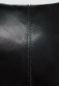 Material de cuero negro con una textura suave, que presenta una costura central y un detalle de costura contrastante.