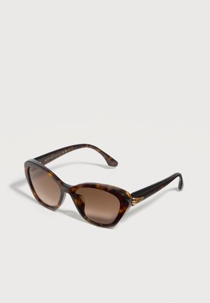 Lunettes de soleil œil de chat écaille avec verres marron dégradés et détails dorés sur les branches, inclinées sur une surface blanche.