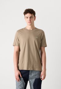 Beige bomulds T-shirt med korte ærmer og rund hals; har et lille grønt "HUGO" logo på brystet; glat tekstur.