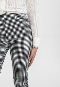 Černobílé kárované kalhoty se slim fit, zkombinované s bílou blůzou s krajkovým lemem a podrobným designem rukávů.