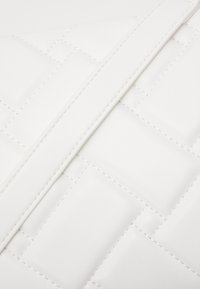 Biała torebka z pikowanej skóry, charakteryzująca się gładką fakturą, skośnym wzorem przeszyć oraz płaskim paskiem.