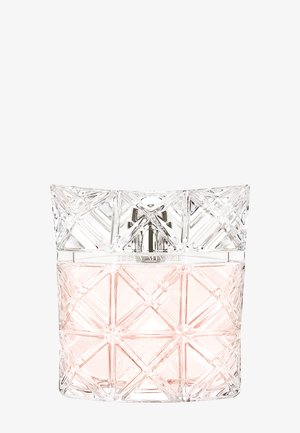 Gjennomsiktig parfymeflaske med geometrisk mønster, fylt med blek rosa væske og sølvfarget spraydyse på hvit bakgrunn.