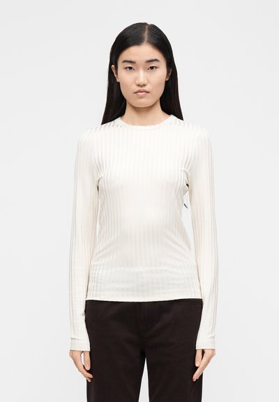 Μπλούζα με μακριά μανίκια, ριμπ ύφανση σε εκρού χρώμα με στρογγυλή λαιμόκοψη. Το ύφασμα φαίνεται λείο και εφαρμοστό, ενώ τα μανίκια στενεύουν στον καρπό.