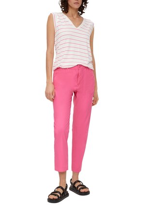 Biała koszulka na ramiączkach w serek w różowe paski, w połączeniu z różowymi, tapered spodniami i czarnymi sandałami. Posiada luźny krój i casualowy design.
