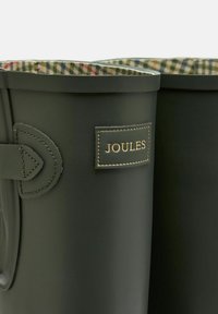 Zielone gumowe kalosze z podszewką w wzór tartan, wyposażone w wytłoczoną metkę z logo oraz dekoracyjne paski po bokach.