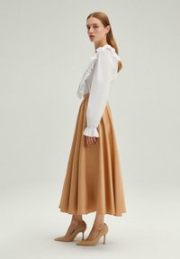 Blusa blanca con detalles de volantes, falda fluida beige y zapatos de tacón nude. Tejido suave, cintura ajustada y ligera campana en el dobladillo.