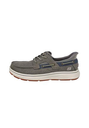 Zapato informal gris con cordones, suela blanca, suela exterior marrón, costura lateral y collar acolchado, visto desde el lado exterior.