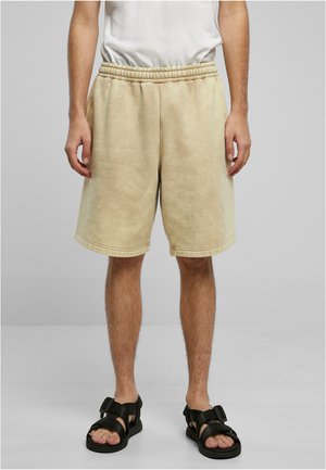 Beige sweat shorts with an elastic waistband, featuring a soft, textured finish and side pockets. Paired with black sandals.