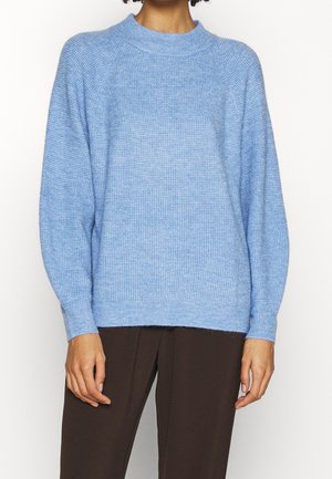 Light blue knitted sweater with long sleeves and round neckline worn with dark brown pants, shown from shoulders to hips.