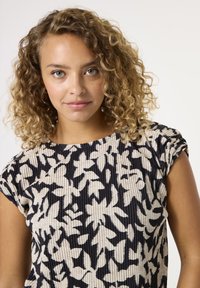Top con estampado floral en color crema y negro, que cuenta con una textura acanalada, mangas cortas y un escote redondeado, enfatizando un ajuste relajado.