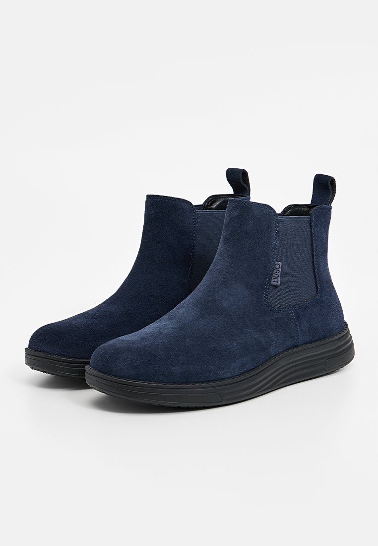 Bottines en daim bleu marine avec panneaux élastiques sur les côtés, languettes de traction, et semelles en caoutchouc noir, arborant une texture lisse et un design simple.