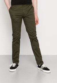 Chinos verde oliva de corte slim, hechos de algodón, con cierre de botón, bolsillos laterales y combinados con zapatillas negras.