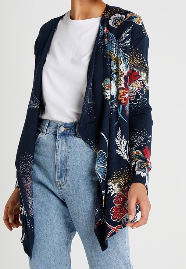 Marinblå långärmad öppen cardigan med flerfärgade blommönster, bärs över en vit t-shirt och ljusblå högmidjade jeans.