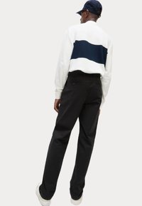 Felpa bianca con una striscia orizzontale blu navy, pantaloni neri e sneakers bianche. Tessuto morbido, vestibilità rilassata e design essenziale.