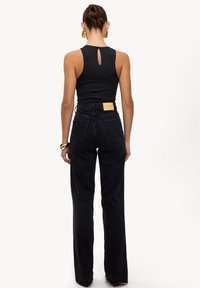 Top negro sin mangas con un corte en forma de llave en la espalda; jeans de mezclilla negros de tiro alto con una etiqueta en la parte posterior, diseño recto y un ligero dobladillo en la parte inferior.