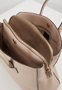 Beżowa skórzana torebka z złotymi akcentami, z zamykaną na zamek kieszenią wewnętrzną oraz przestronnymi przegródkami. Teksturowane, gładkie wykończenie.