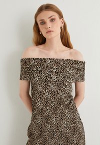 Leopardenmuster-Kleid mit schulterfreier Form, aus weichem Stoff gefertigt, mit tailliertem Design, Raffung und einem hellbraunen Hintergrund.