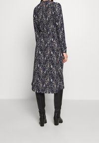 Granatowa sukienka z długimi rękawami, zdobiona wzorem paisley. Długość do połowy łydki z wysmuklonym talią, zestawiona z czarnymi wysokimi botkami.