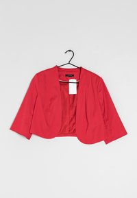 Veste rouge courte avec des manches trois-quarts, texture lisse et devant ouvert. L'intérieur présente un motif à pois. Étiquette attachée.