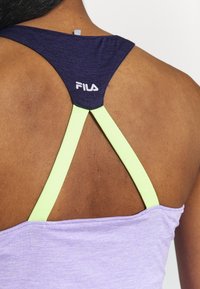 Lila idrottstankini med en mörkblå och neongrön korsad baksida. Har en logotyp nära axeln och en mjuk, slät textur.
