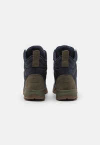 Bottes de randonnée imperméables bleu marine foncé avec des accents verts, dotées d'un col rembourré, d'un tissu texturé et d'une semelle robuste avec des motifs de grip.