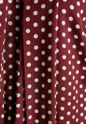 Burgundi kangas valgete täppidega, millel on sile tekstuur ja volditud disain, näidates ühtlast mustrit erineva suurusega täppidega.