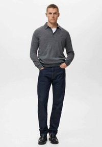 Polo cu tricot gri, blugi bleu închis, cizme negre. Croi slim, design minimalist, manșete și guler cu costiță. Fără modele sau accente vizibile.