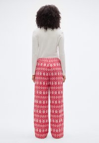 Pantalon de pyjama à motifs rouges avec des dessins floraux blancs et des losanges, présentant une silhouette à jambes larges et une taille élastique.