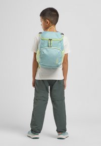 Zaino di colore azzurro chiaro con dettagli gialli, numerosi scomparti, tasche laterali in rete e spallacci imbottiti. Indossato da un bambino.
