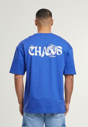 Blå bomulds t-shirt med korte ærmer, med stort hvidt "CHAOS" tekst på ryggen og en bølgeskabelon, afslappet pasform og rund hals.