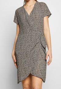 Robe à motif noir et blanc avec un décolleté en V, des manches courtes, un design croisé et un ourlet légèrement courbé, fabriquée en tissu léger.