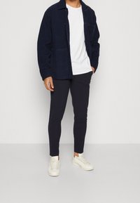 Marinblå sammetsjacka med en vit t-shirt, kombinerad med slim-fit marinblå byxor och krämfärgade sneakers, med en avslappnad design och två fickor.