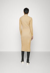 Abito in maglia a coste, aderente, di colore beige, con collo alto, maniche lunghe e tasche laterali, abbinato a stivali neri in pelle aderenti e tacchi a piattaforma.