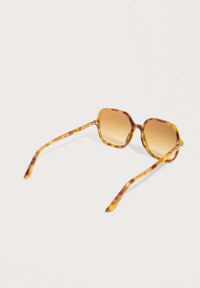 Lunettes de soleil à motif écaille de tortue avec des verres carrés brun dégradé et des branches fines reposant sur une surface claire.